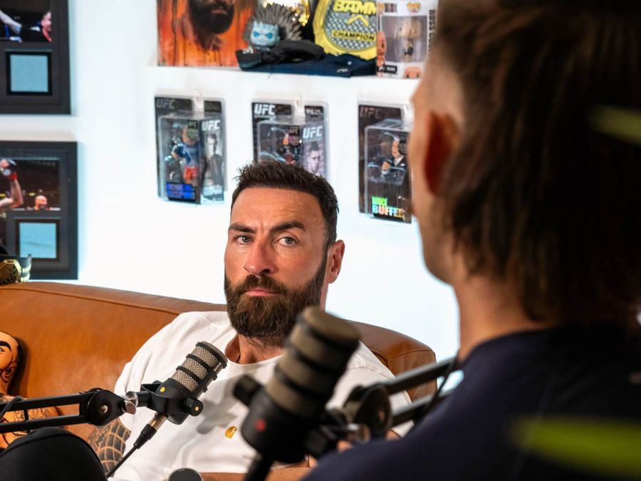 Greg producing a podcast with a guest in a room of UFC memorabilia
